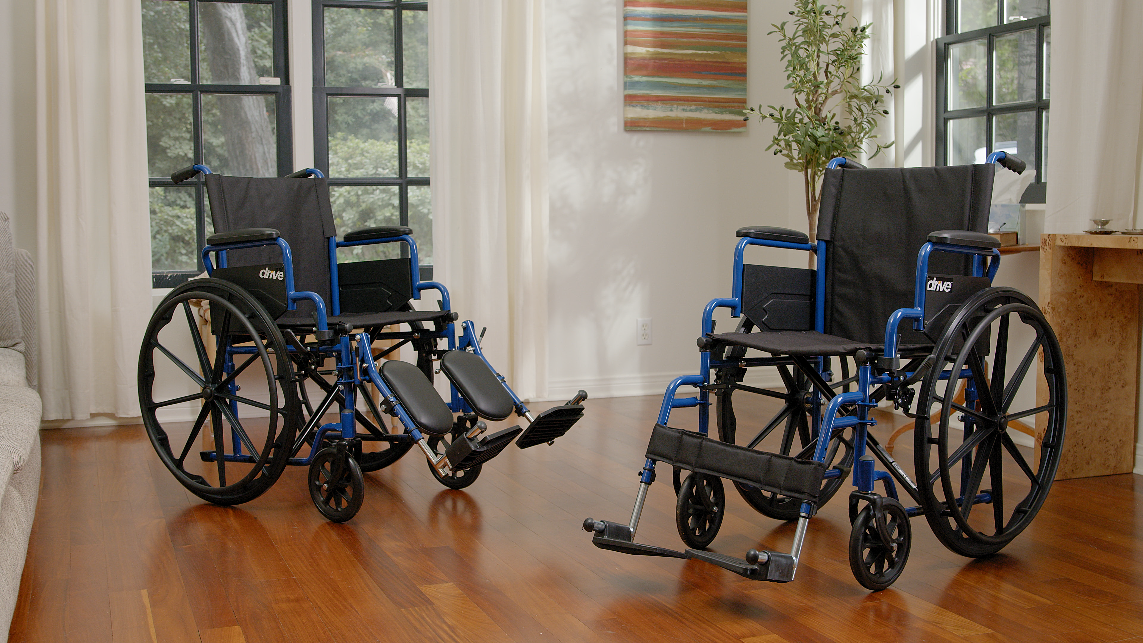Two wheelchairs on a wooden floor with large windows in the background