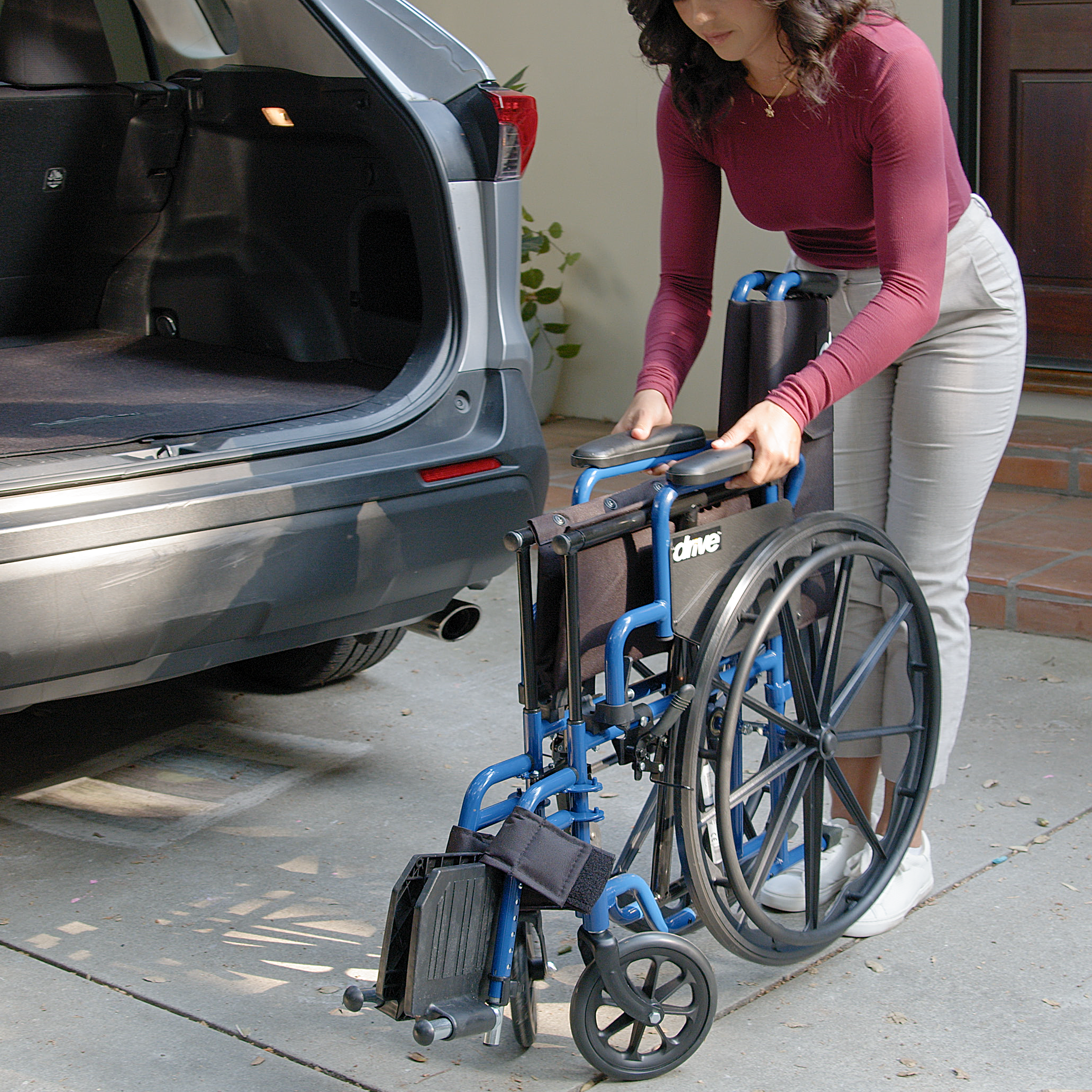 Person pushing a wheelchair towards an open car trunk.