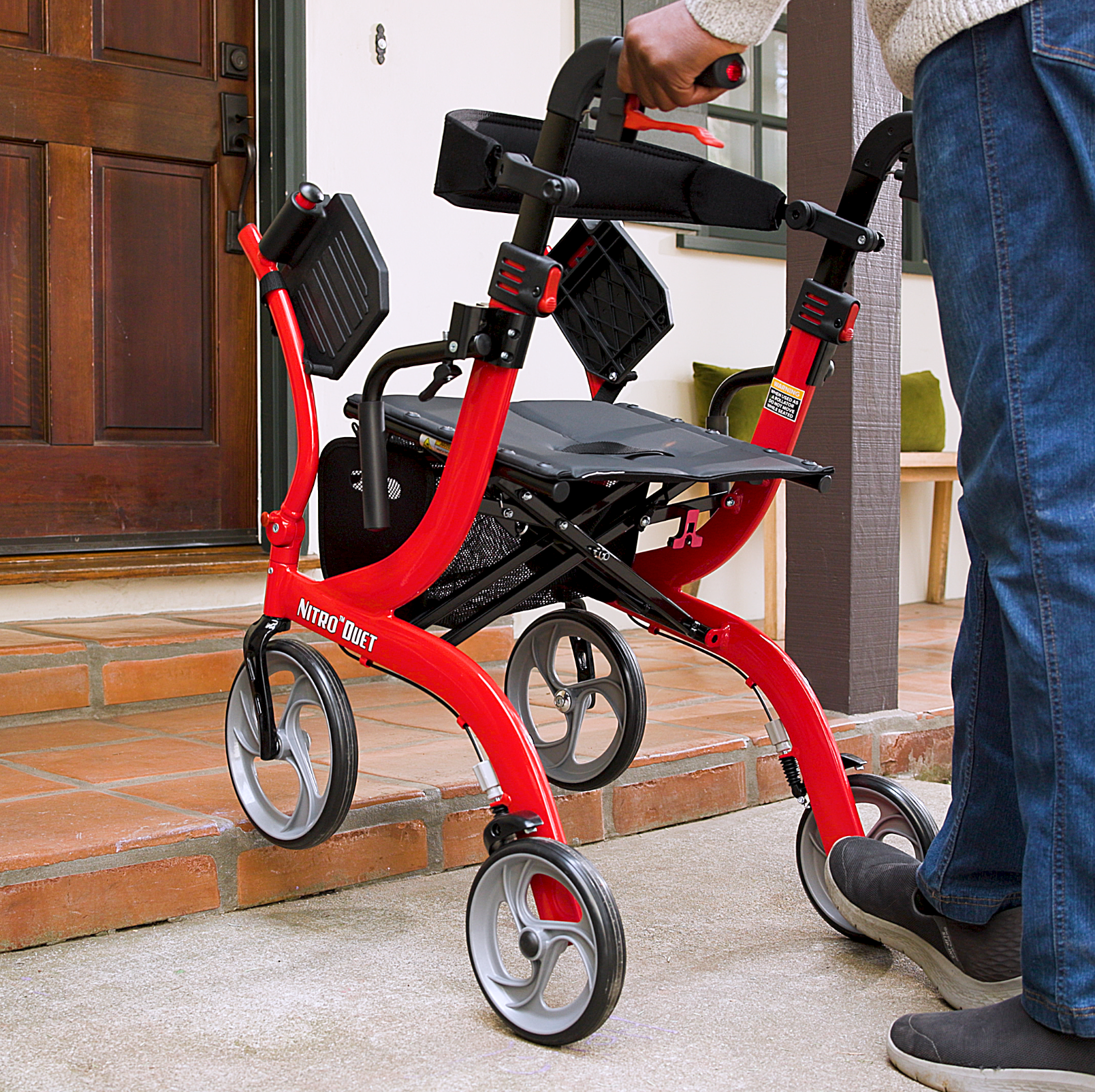 Person holding a red Nitro scooter on a sidewalk.